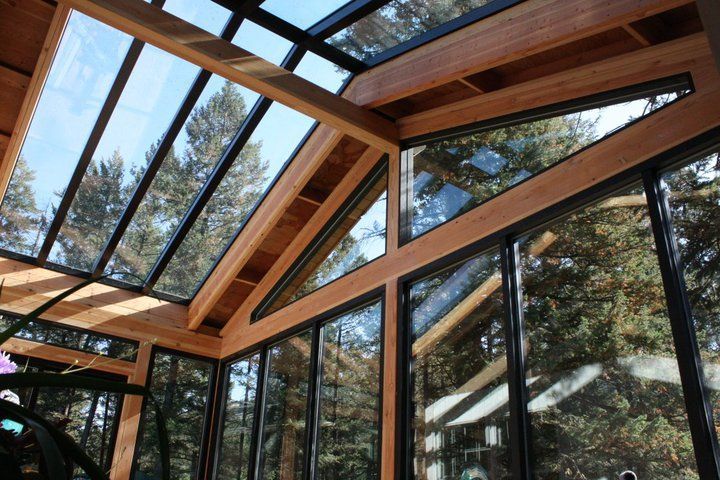 Sunroom with glass roof and walls, wooden beams, trees visible outside.