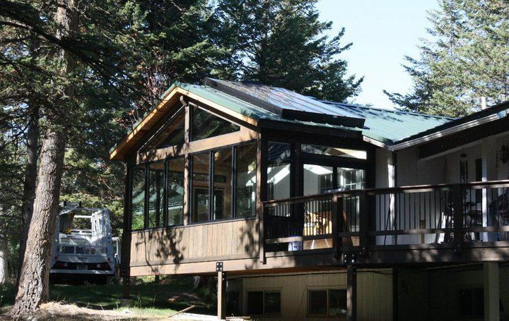 Sunroom with solar panels on a house with a wooden deck. Surrounded by trees, a white van is parked.