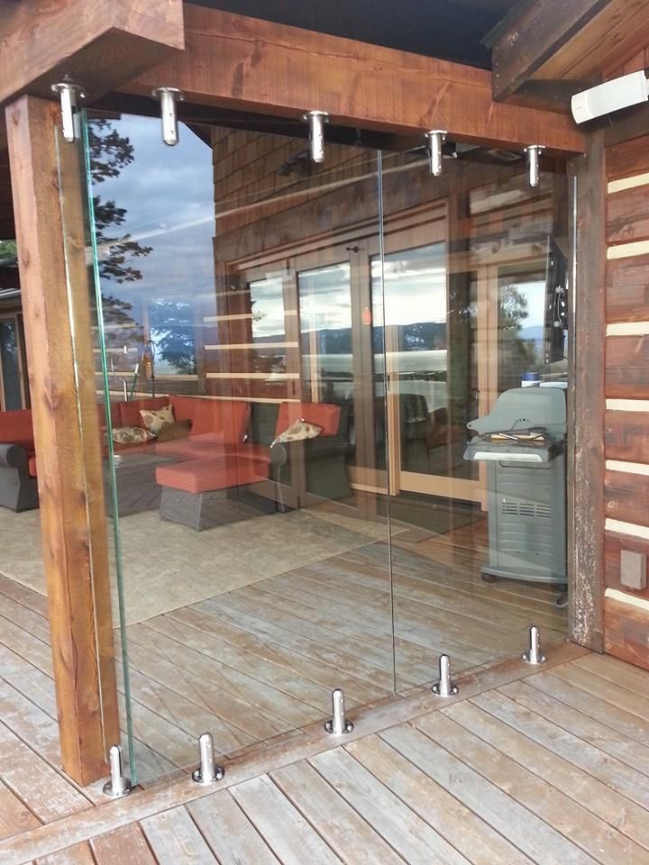 Glass panel railing on a wooden deck, with stainless steel supports, overlooking a water view.