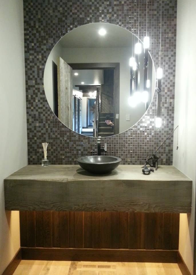 Modern bathroom with round mirror, mosaic tile backsplash, concrete countertop, and wooden paneling.
