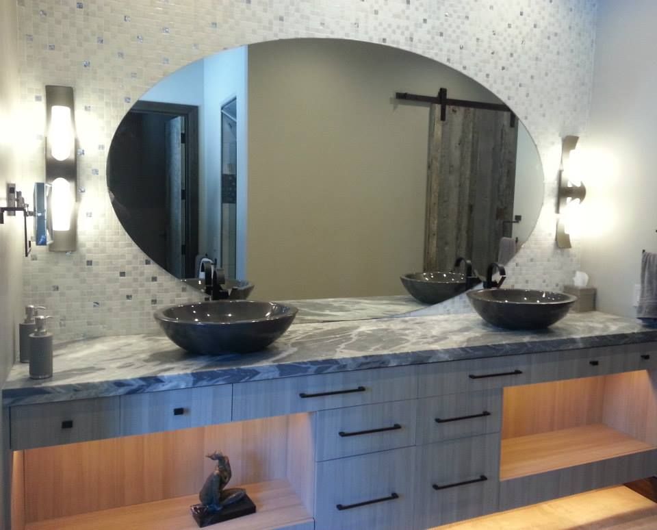 Bathroom with oval mirror, two sinks, gray cabinets, and barn door.