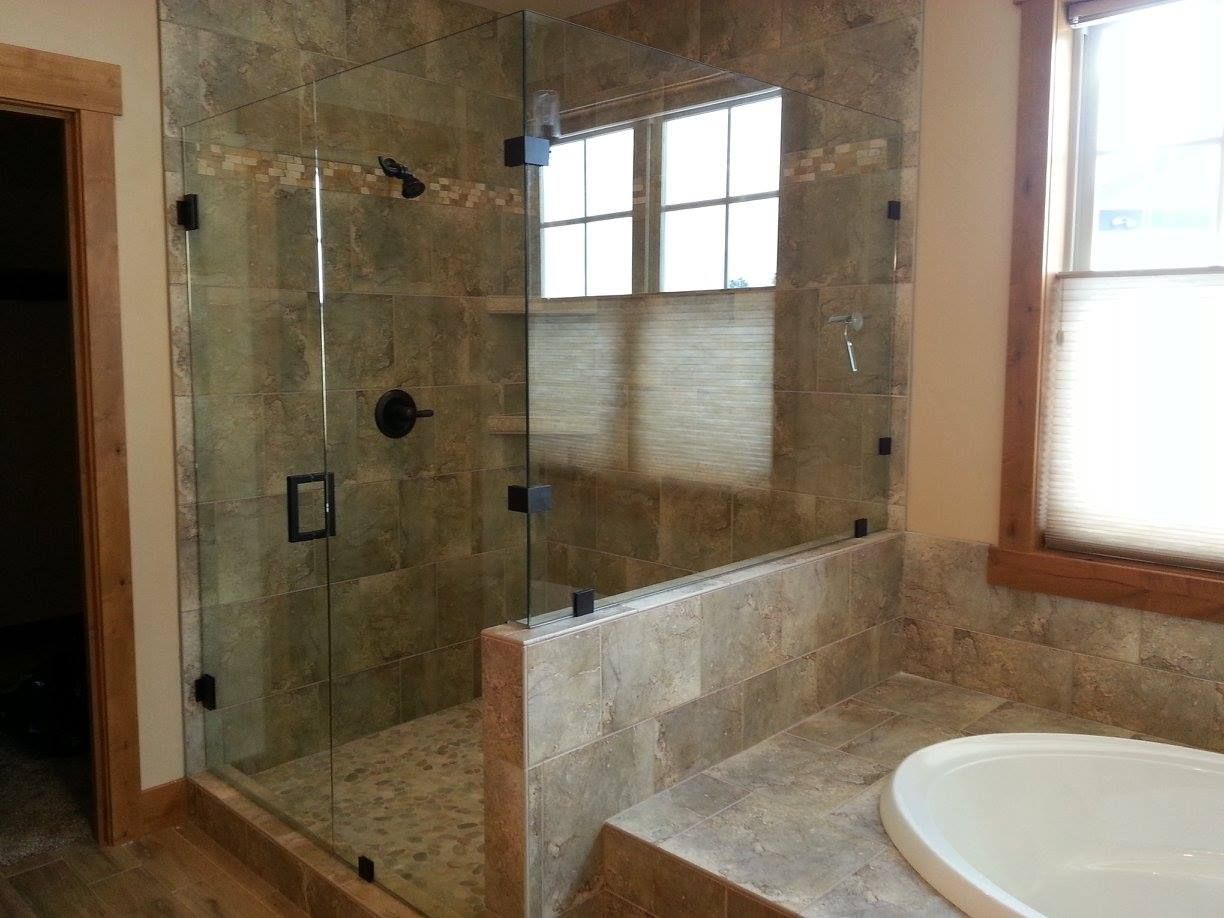 Glass shower enclosure with tile walls and built-in bench, adjacent to a bathtub.