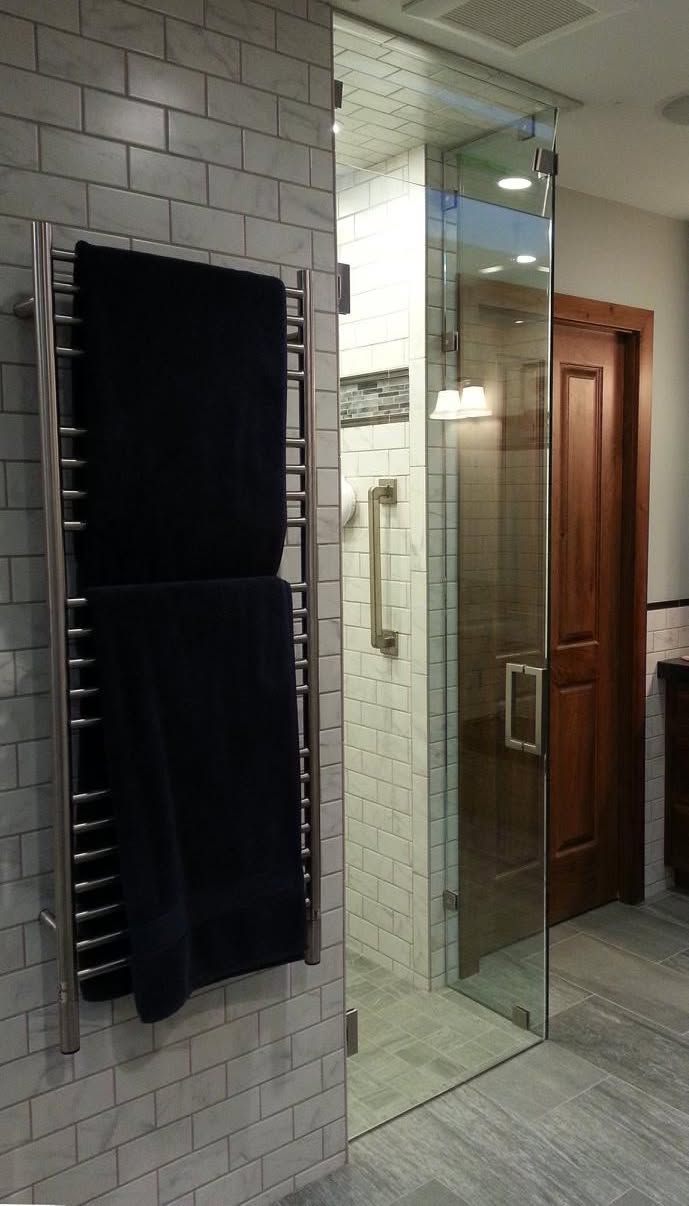 Towel warmer with two dark blue towels, next to a glass shower door, inside a bathroom with light tile.