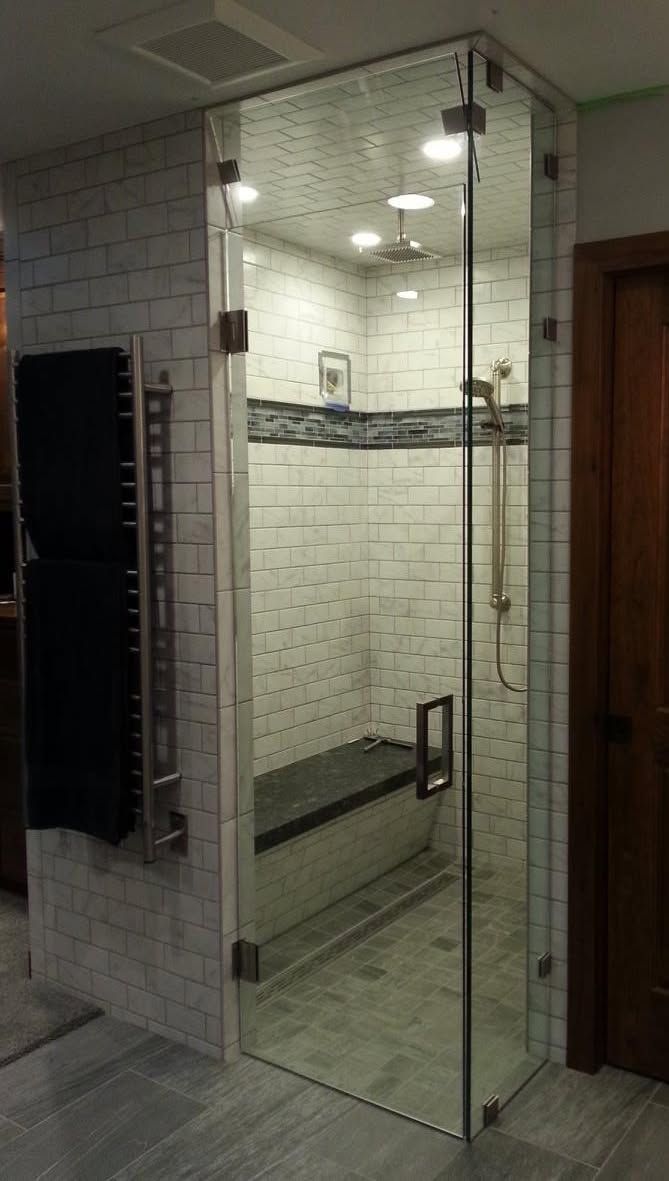 Glass shower enclosure with bench and heated towel rack. White and gray tile with dark accents.