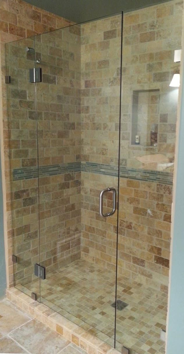 Glass shower enclosure with tan brick-like tile, a small built-in shelf, and a door with a silver handle.