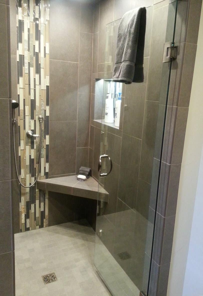 Modern tiled shower with glass door, built-in bench, shelf, and mosaic accent wall.