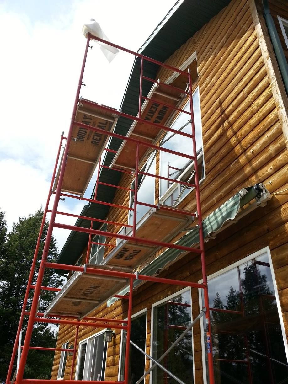 Red scaffolding against a log cabin, set up for work on the roof and windows.