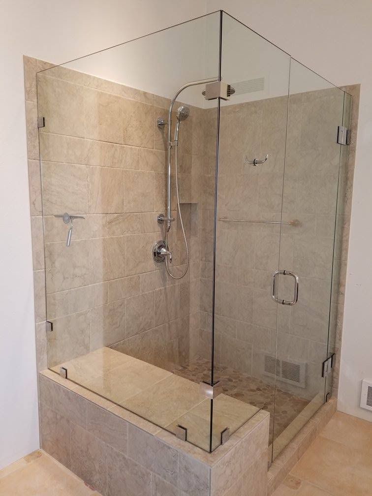 Glass-enclosed shower with beige tile walls, a glass bench, and a silver showerhead.