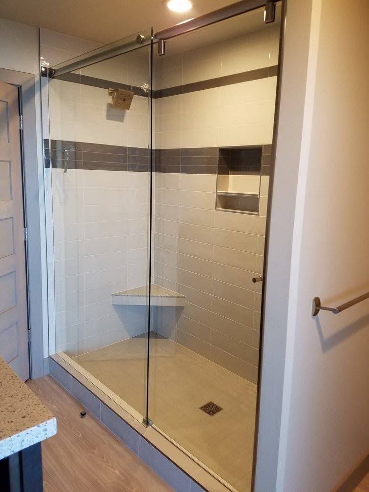 Glass shower enclosure with white, gray, and beige tile. Includes a bench and small shelf.