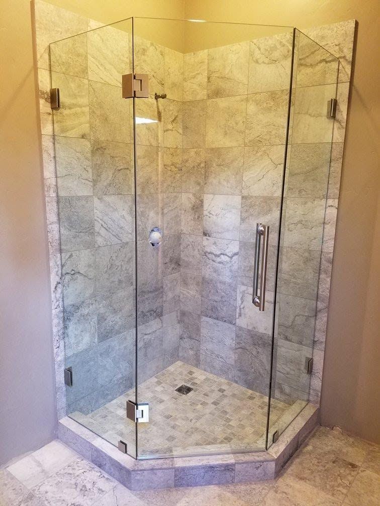 Glass shower enclosure in a corner, with stone tile walls and a door.