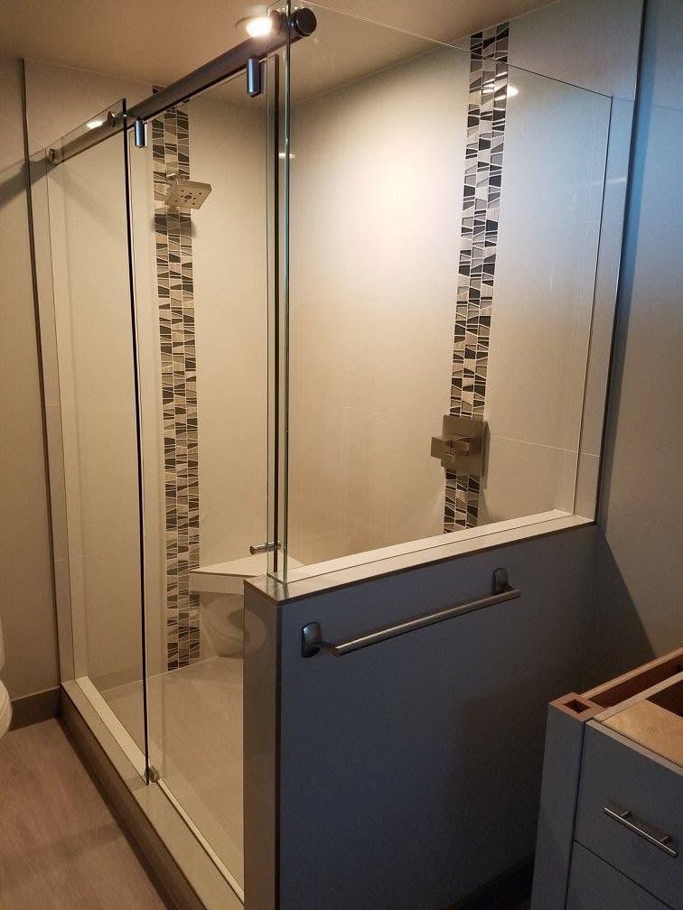 Glass shower stall with sliding door, tile accents, and a towel bar; neutral colors.