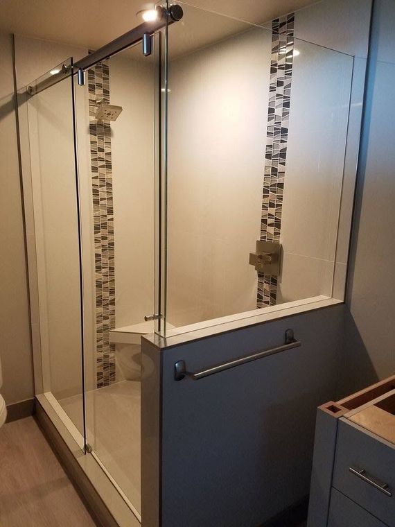 Modern glass shower with tiled accents; towel bar on gray wall, cabinet visible.