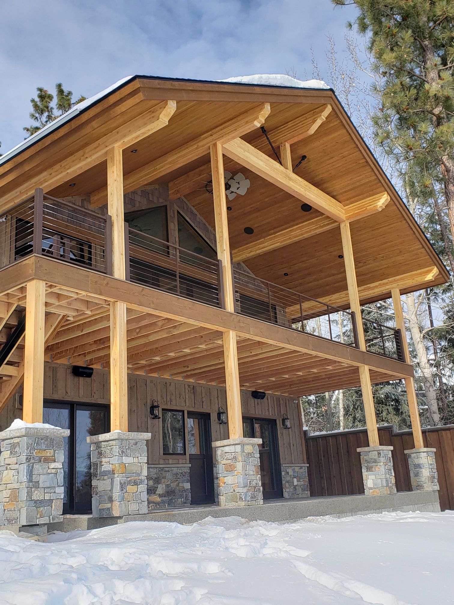 Two-story wood cabin with stone accents, snowy surroundings. Wooden pillars support the porch and balcony.