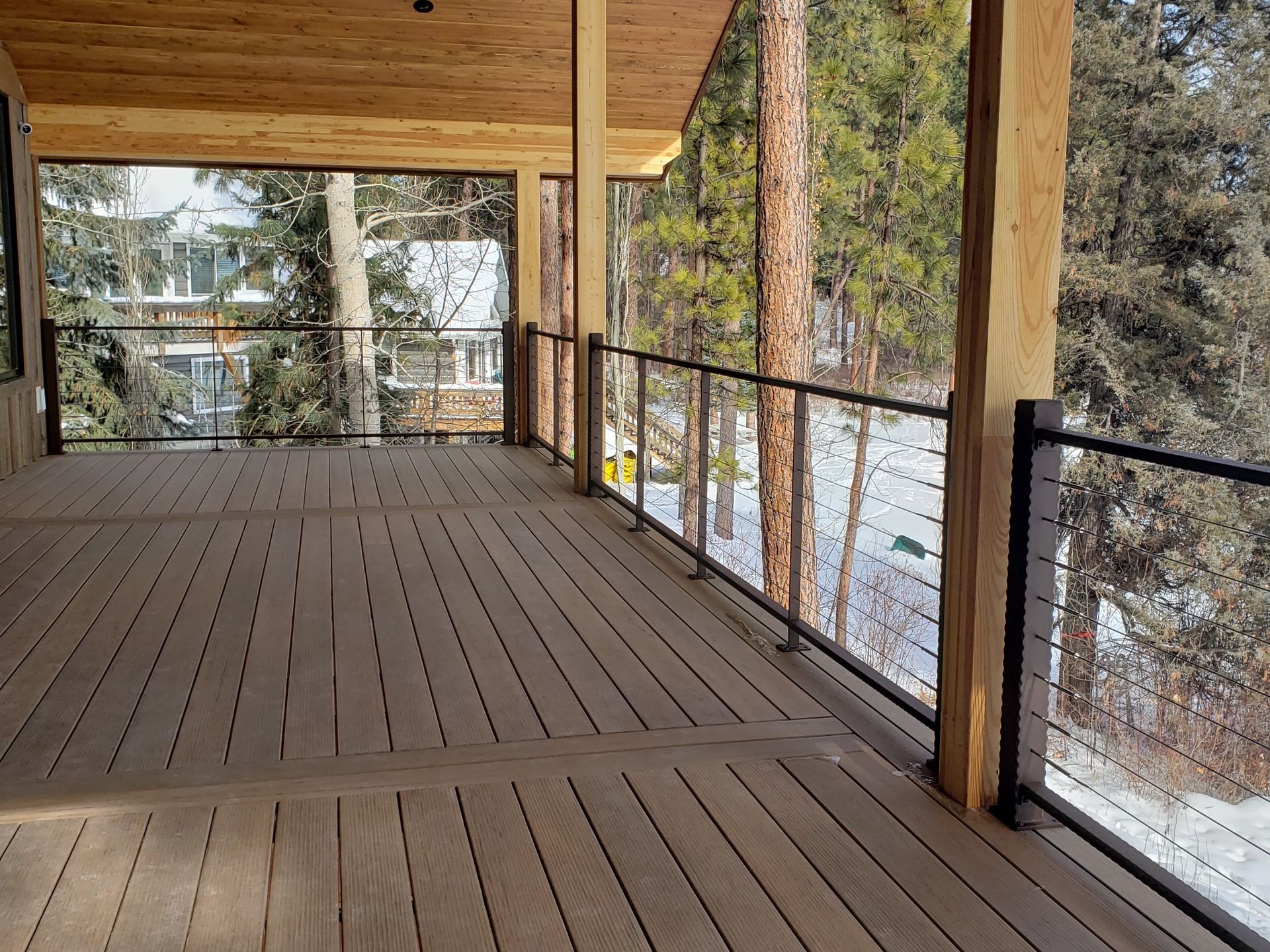 Wooden deck with cable railings, overlooking a snowy landscape and trees.