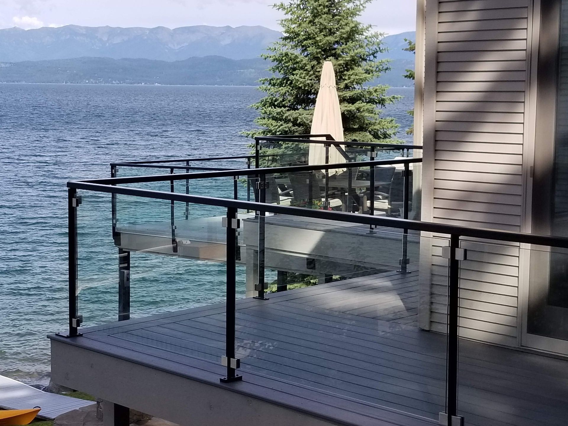 Deck overlooking a lake with glass railings and a black handrail.