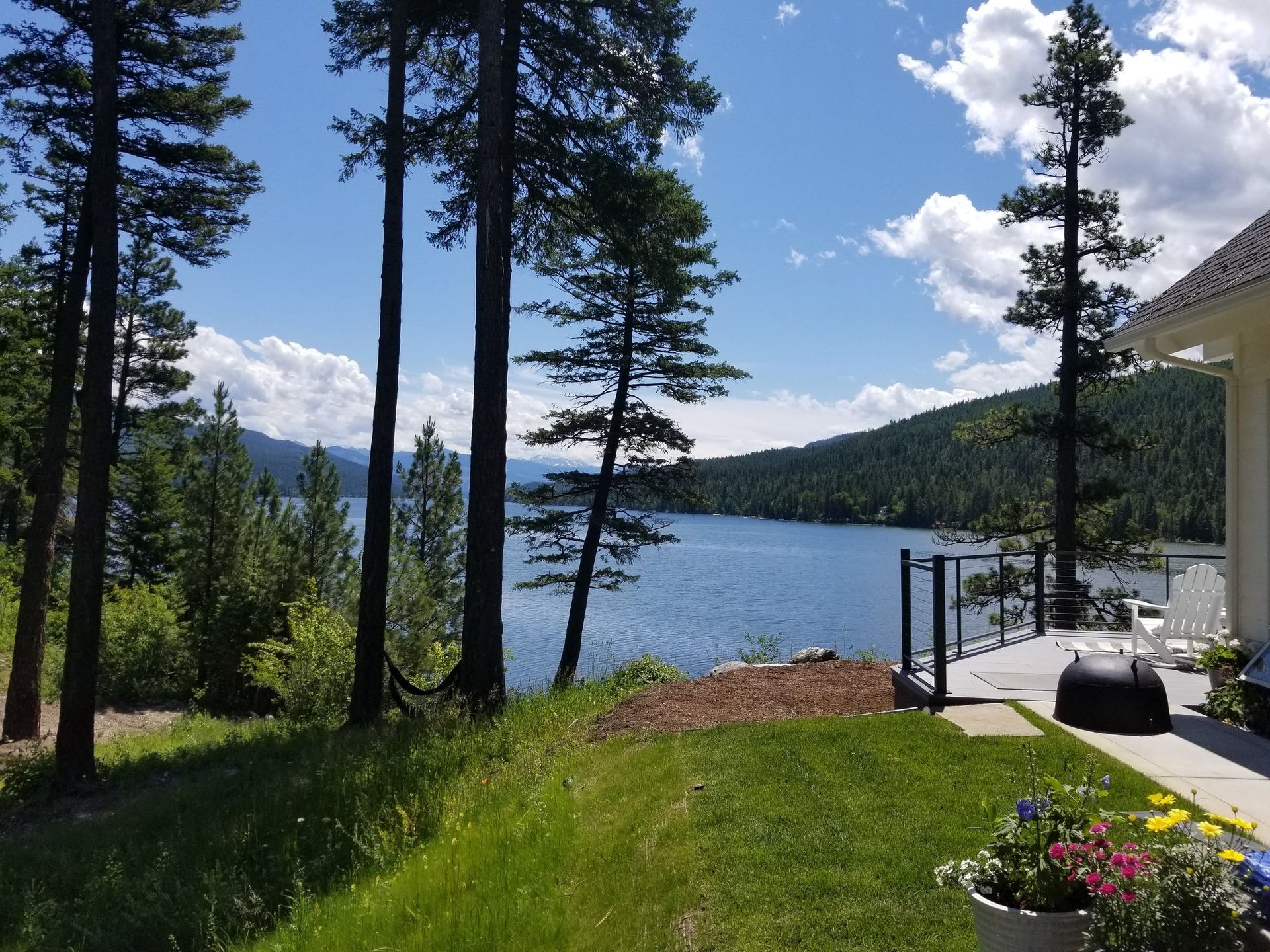 Lakeside view with trees, blue water, and a deck in the sun under a partly cloudy sky.