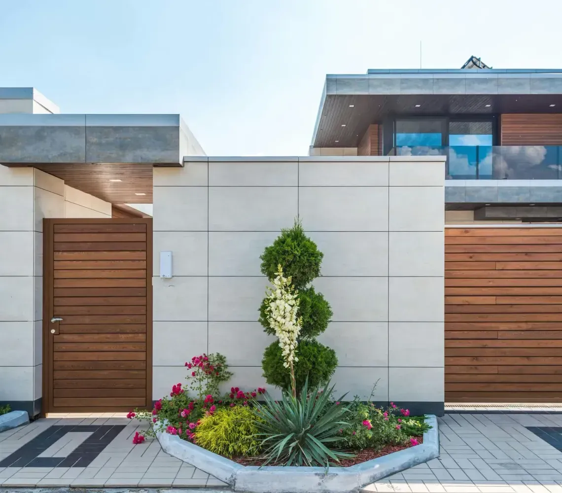 Modern house facade with wood doors, stone walls, and landscaped flower beds
