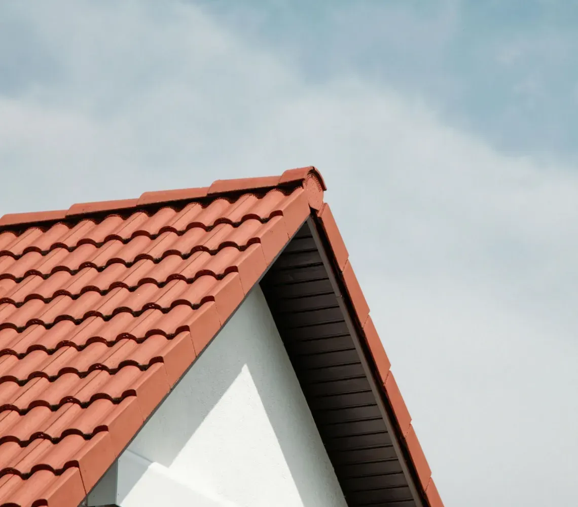 Red-tiled gabled roof against a blue sky with a small dormer window