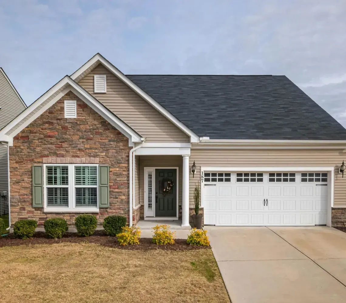 Single-story brick house with gray roof, white garage, and front lawn in a suburban neighborhood