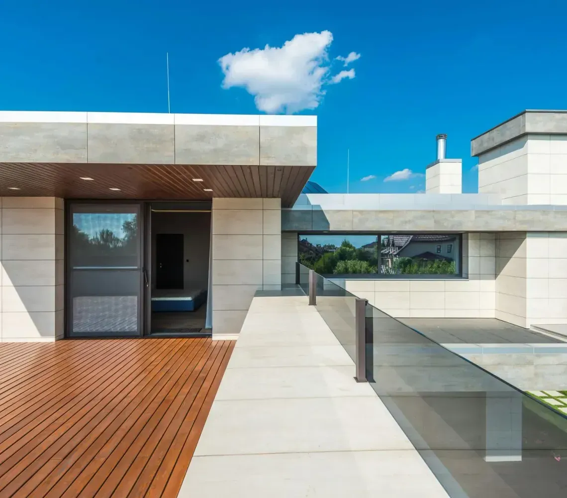 Modern house patio with wood deck, glass railing, and open doorway under a blue sky