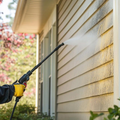 Person pressure washing beige house siding with a spray wand