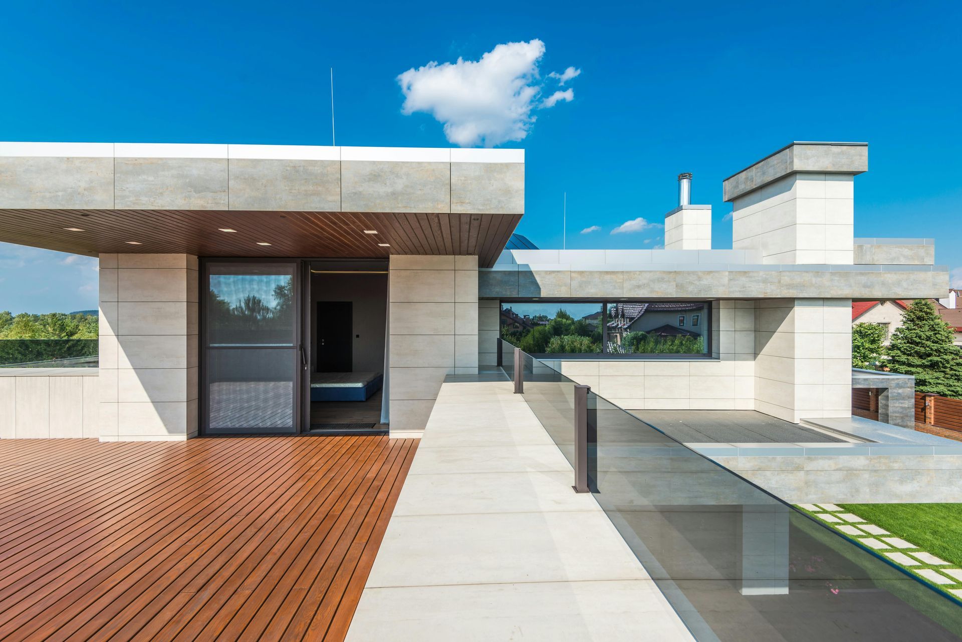 Modern house patio with wood deck, glass railing, and open doorway under a blue sky
