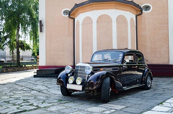 An old black car is parked in front of a building.