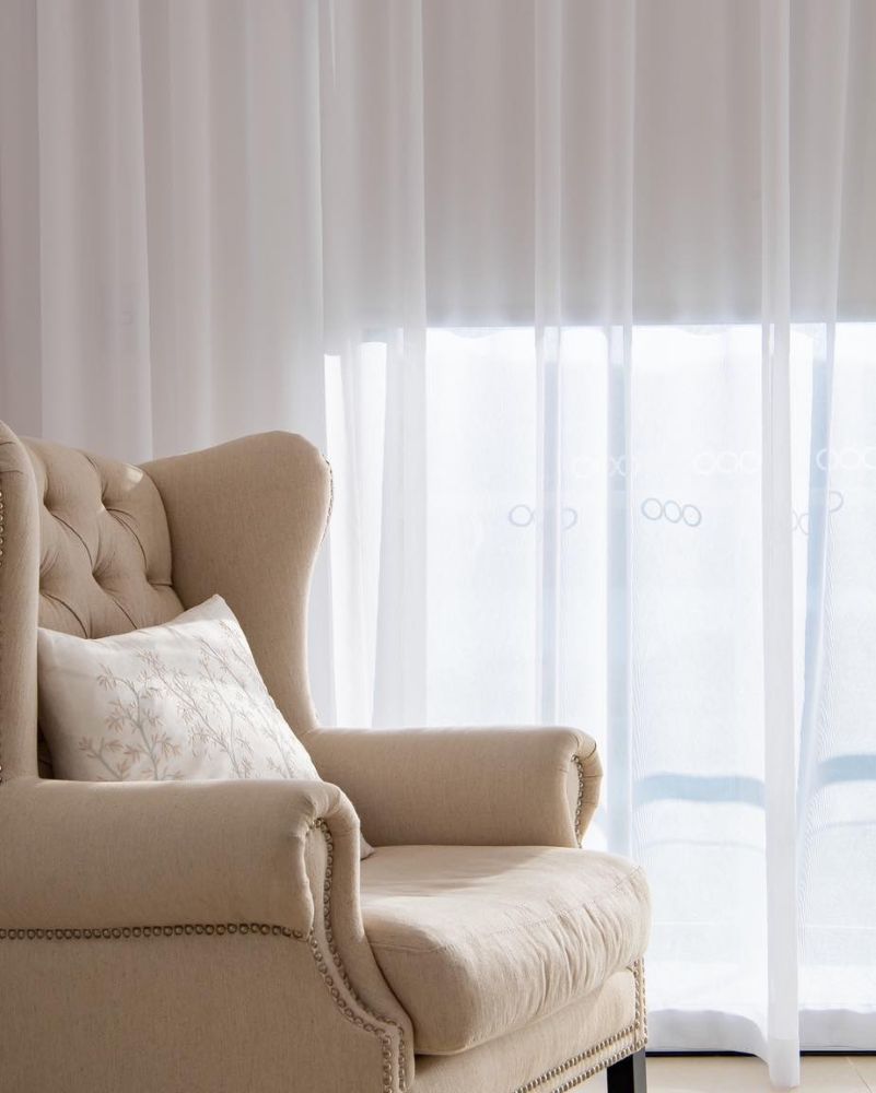 A Chair is Sitting in Front of a Window With White Curtains — Whitsunday Vogue Interiors in Airlie Beach, QLD