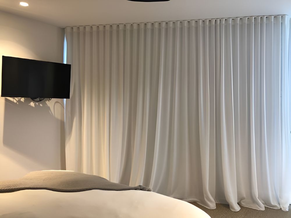 A Bedroom With White Curtains and a Flat Screen TV — Whitsunday Vogue Interiors in Bowen, QLD