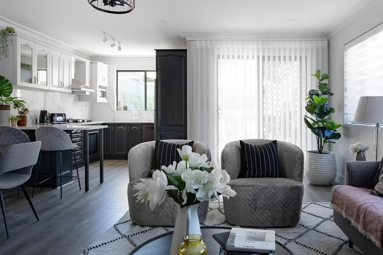 Living Room With Kitchen, Gray Armchairs, Black and White Cabinets, and White Curtains — Whitsunday Vogue Interiors in Cannonvale, QLD