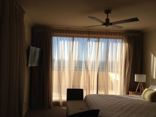 Bedroom With Sheer Curtains, Sunlight Streaming Through Large Window, and a Ceiling Fan — Whitsunday Vogue Interiors in Cannonvale, QLD