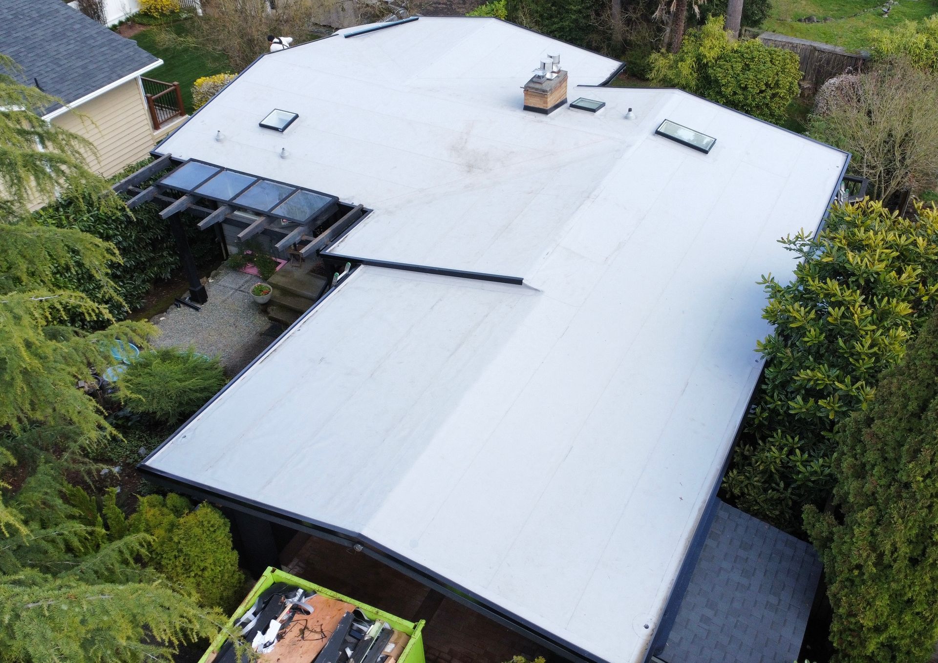 An aerial view of a house with a white roof surrounded by trees.