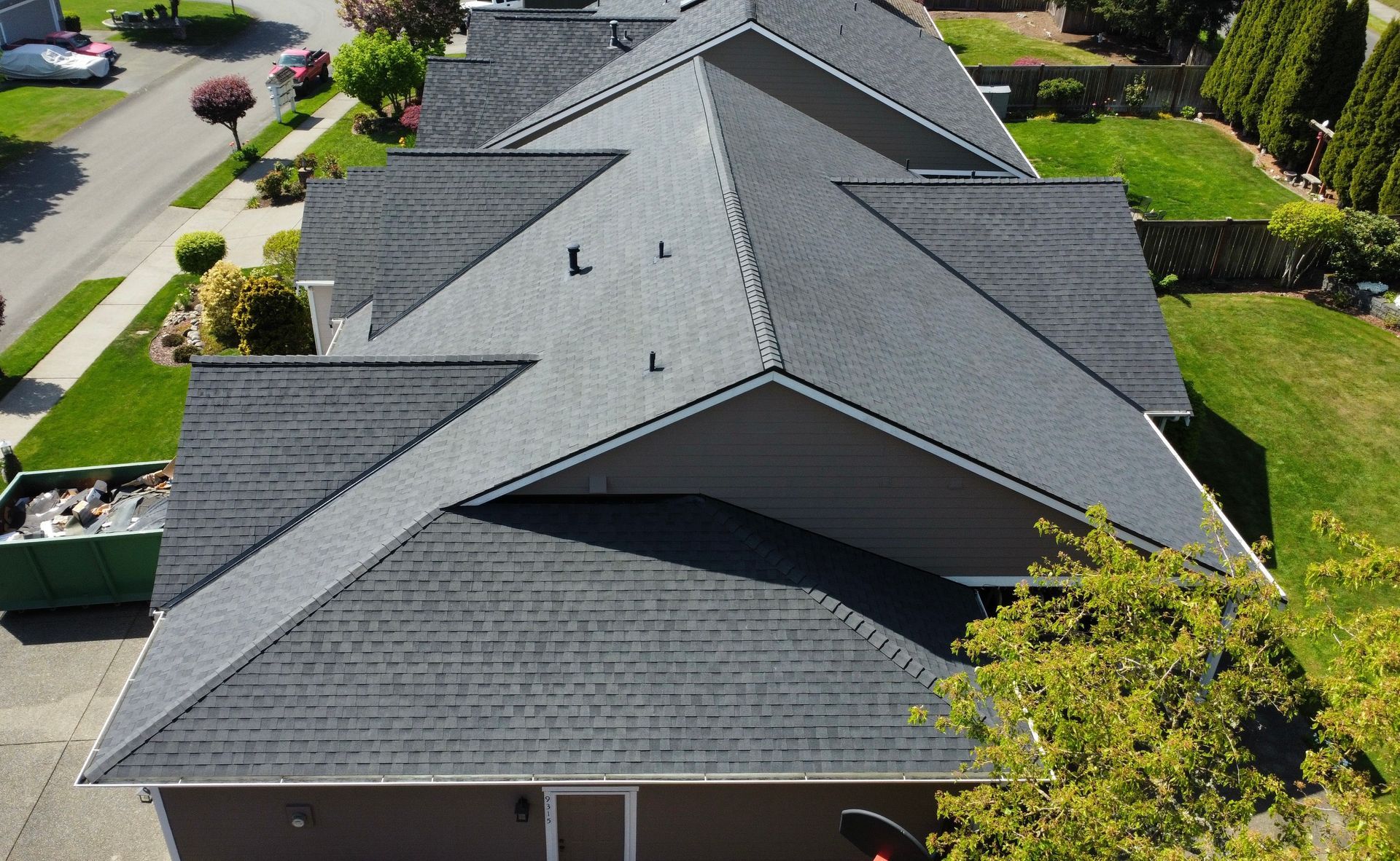 Aerial view of a gray-shingled suburban house with a landscaped yard and street nearby.