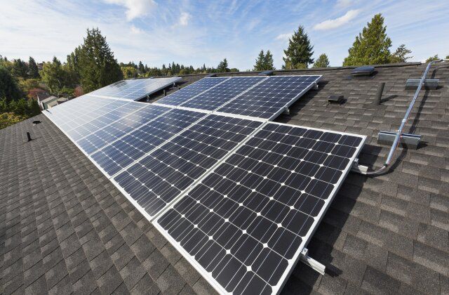 A row of solar panels on a roof with trees in the background