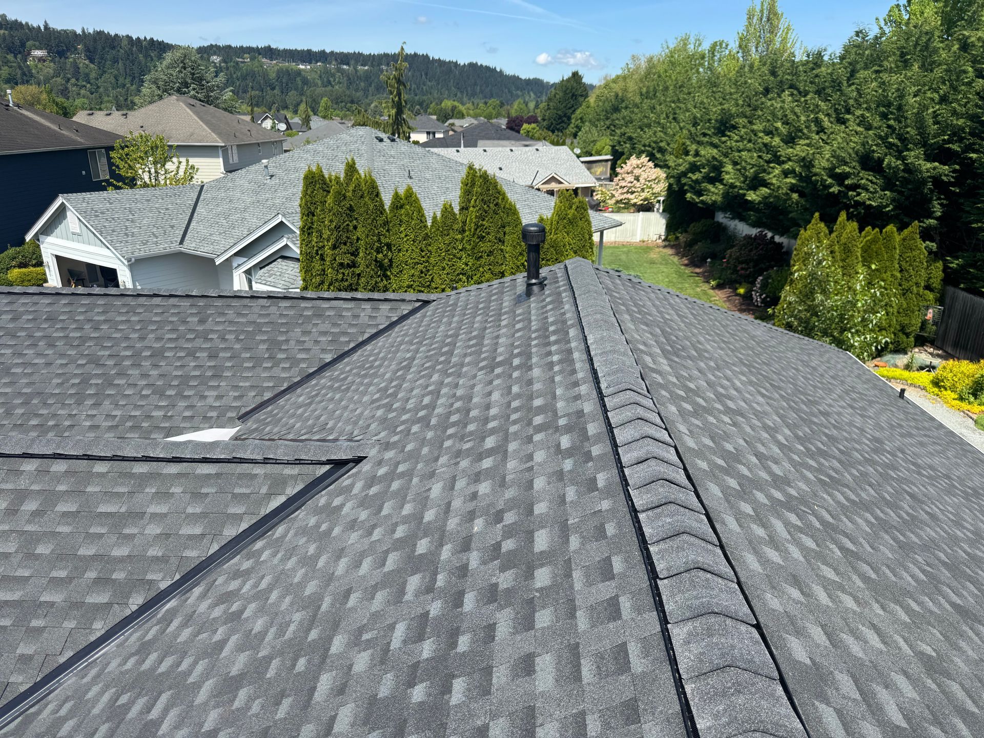 The roof of a house with a gray shingle roof is surrounded by trees and houses.