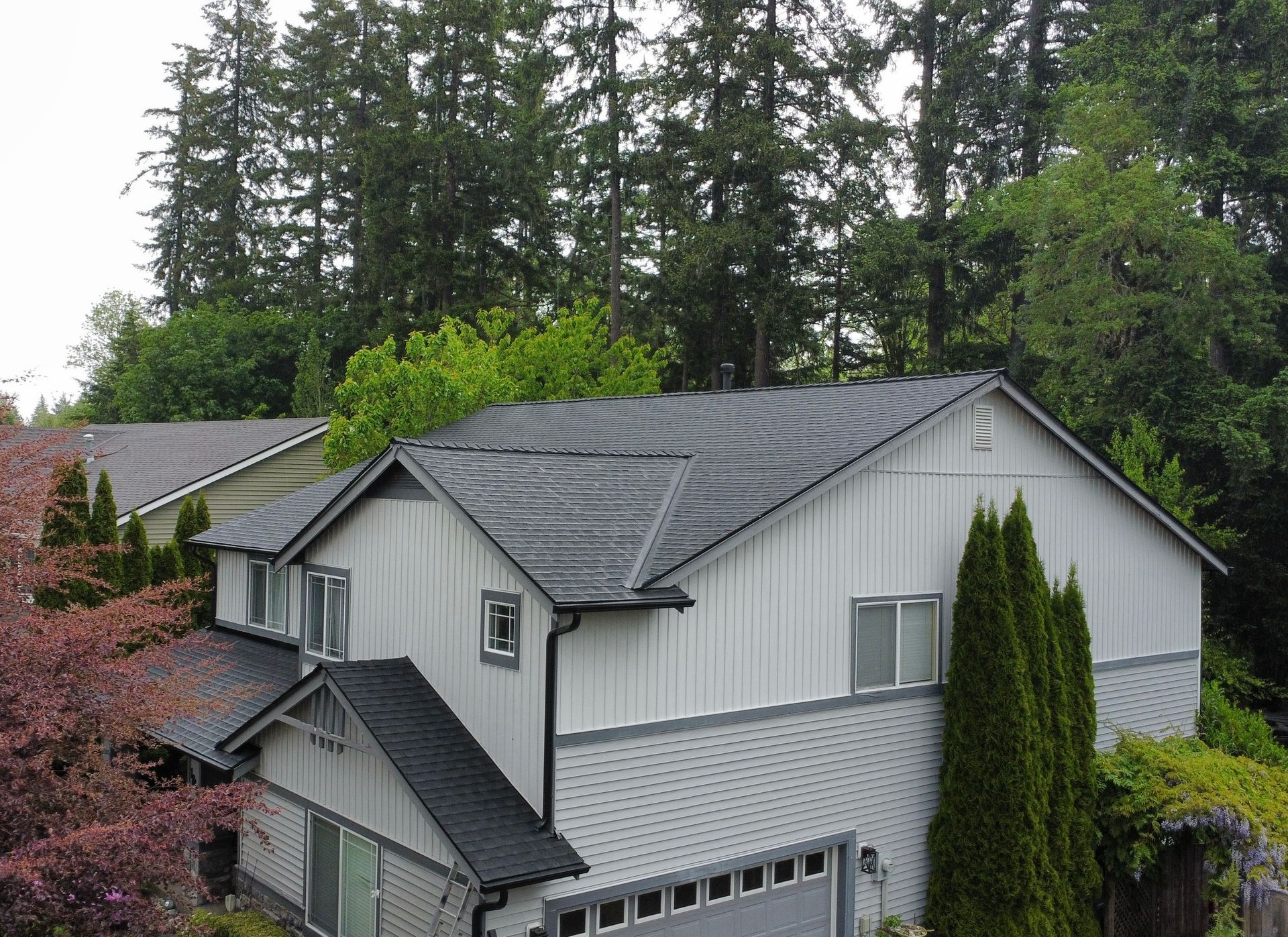 A white house with a black roof is surrounded by trees