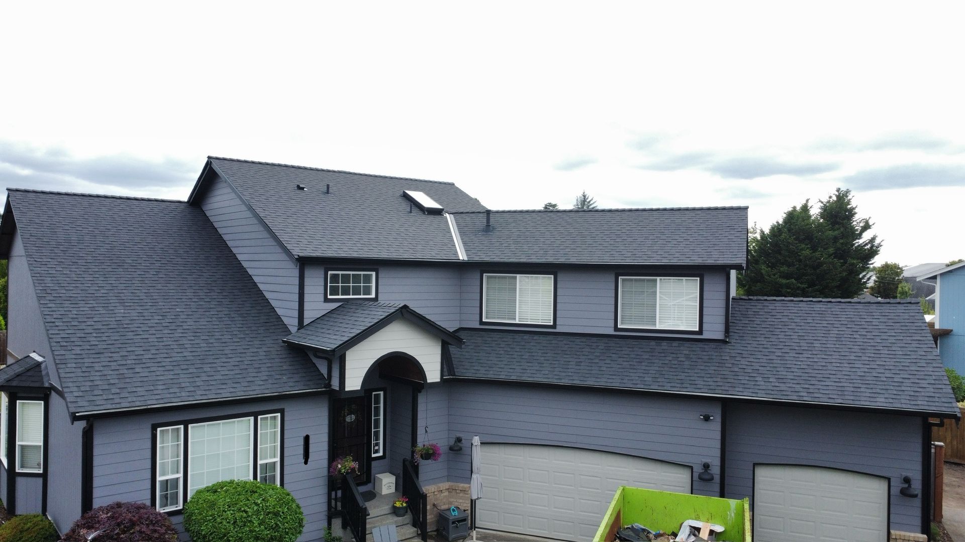 A large gray house with a green dumpster in front of it