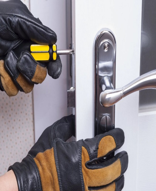 A person wearing gloves is using a screwdriver to fix a door handle