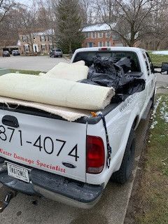 A white truck with a rug in the back is parked on the side of the road.