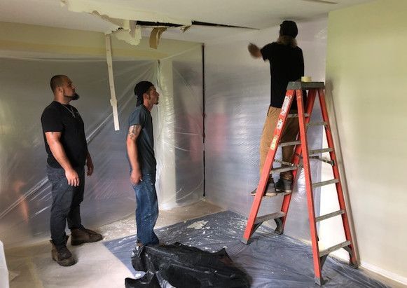 Three men are standing in a room with a ladder.