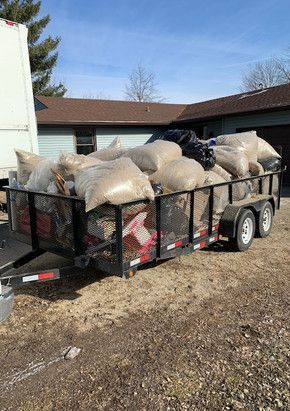 A trailer filled with bags of trash is parked in front of a house.
