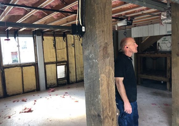 A man is standing in an empty room next to a wooden pillar.