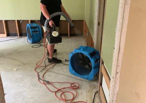 A man is using a vacuum cleaner and a fan in a room.
