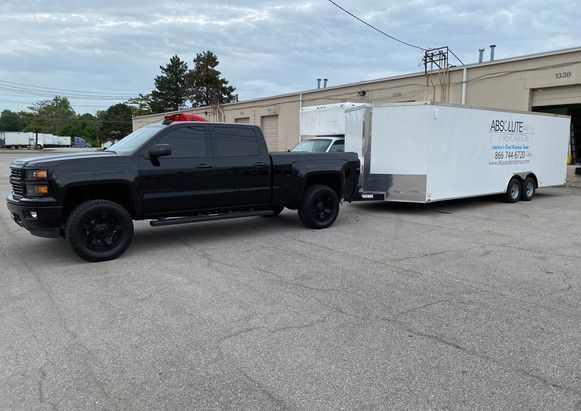 A black truck is towing a white trailer in a parking lot.