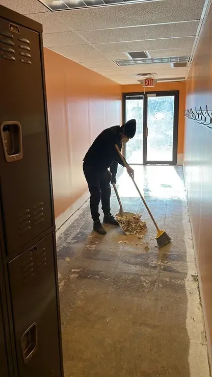 A man is sweeping the floor of a hallway next to a locker.