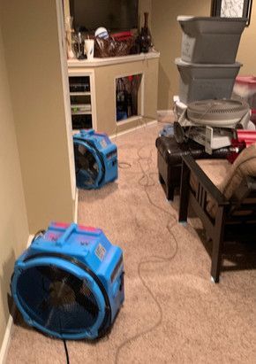 Two blue fans are sitting in a living room next to a stack of boxes.
