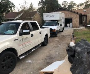 Two white trucks are parked in front of a house.