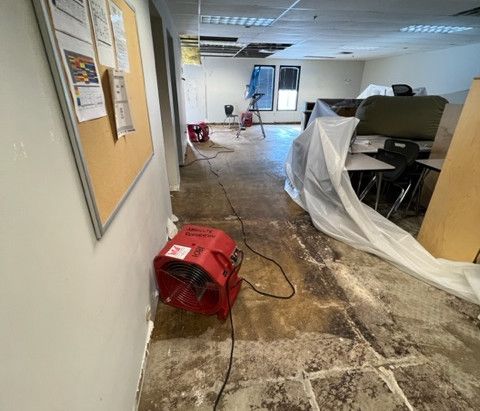 A red fan is sitting in a hallway next to a bulletin board.