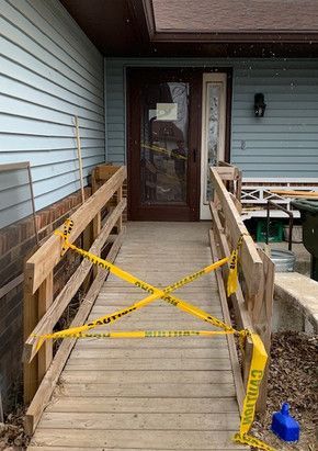 A wooden ramp with yellow tape on it is leading to the front door of a house.