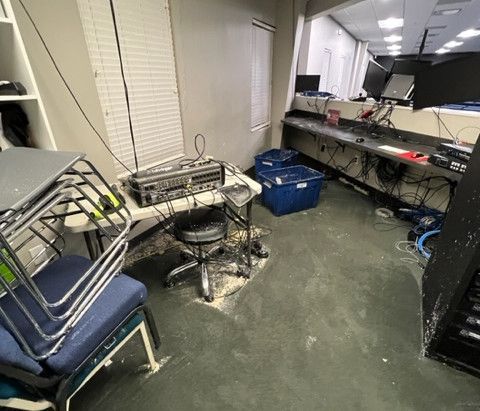 A room with a stack of chairs , a desk , a stool , and a computer.